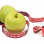 two green apples with a measuring tape around them
